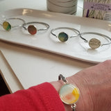 Silver colored stainless  bracelet with a round watercolor style blue/orange/pink gem on the center