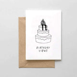 A white card with a black text: "BIRTHDAY VIEWS" and an illustration of a man sitting on a cake. Comes with a brown envelope.