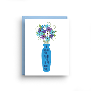 A white card with a text: "I HEAR YOU AND I'M HERE FOR YOU" and an illustration of a blue flowers in a blue vase." Comes with a light blue envelope.
