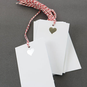 A white gift tag with red/white strings with an illustration of a silver heart on top.