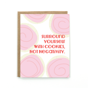 A white card with a pink text: "SURROUND YOURSELF WITH COOKIES. NOT NEGATIVITY" and an illustration of pink cookies.